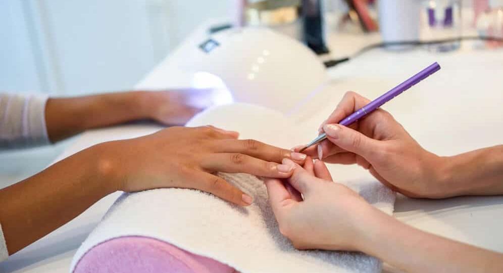Manos de una profesional realizando un servicio de manicura a una mujer en un centro de estética